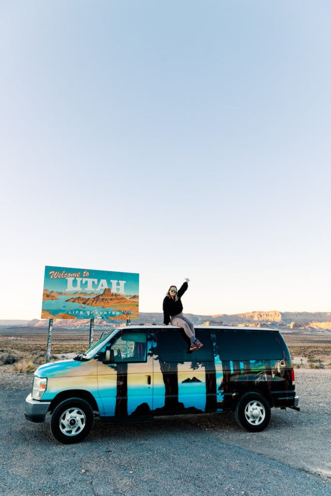 Girl sitting on top of van in front of Utah sign