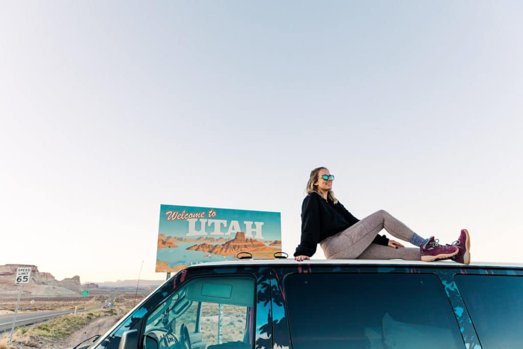 girl sitting on top of van in front of Utah sign