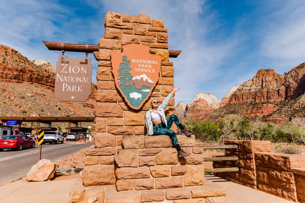 girl sitting in front of Zion National Park sign