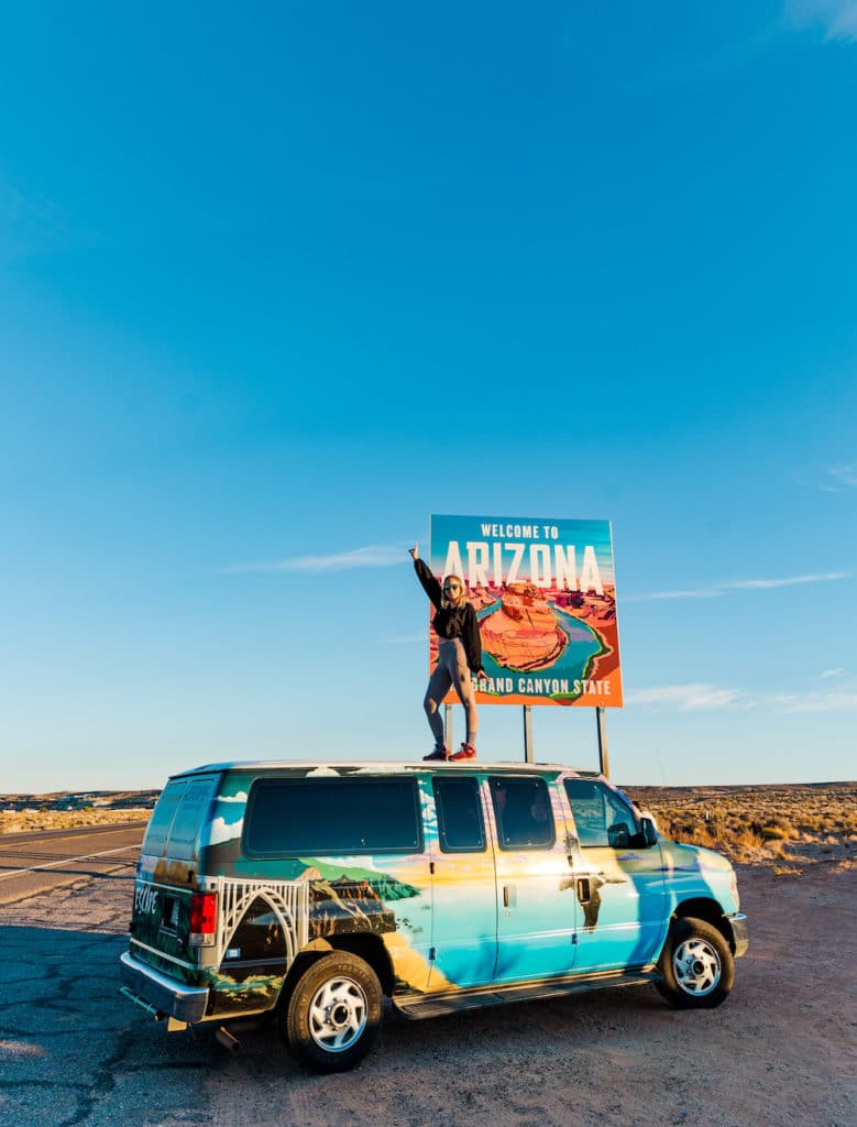 Girl standing on top of van in front of Arizona sign