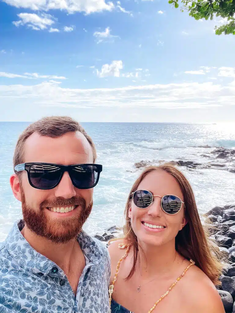 man and woman in sunglasses smiling at the camera with ocean in the background. Taken at the Voyagers of the Pacific Luau at the Royal Kona Resort on the Big Island of Hawaii