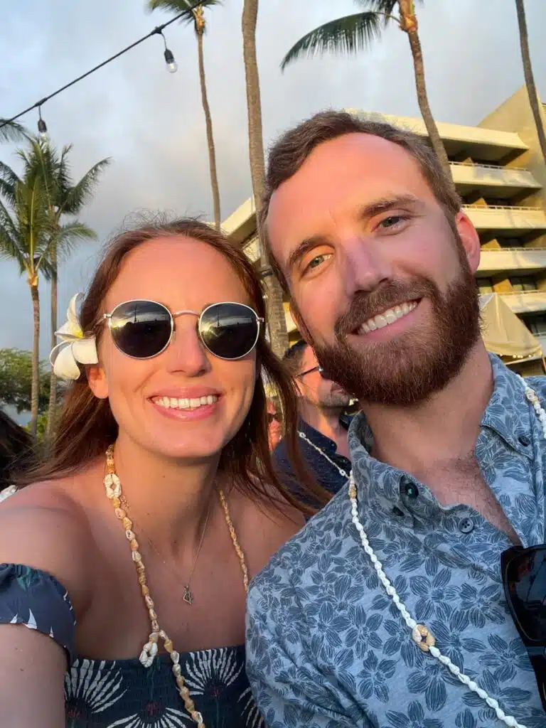 man and woman in smiling at the camera with hotel and palm trees in the background. Taken at the Voyagers of the Pacific Luau at the Royal Kona Resort on the Big Island of Hawaii