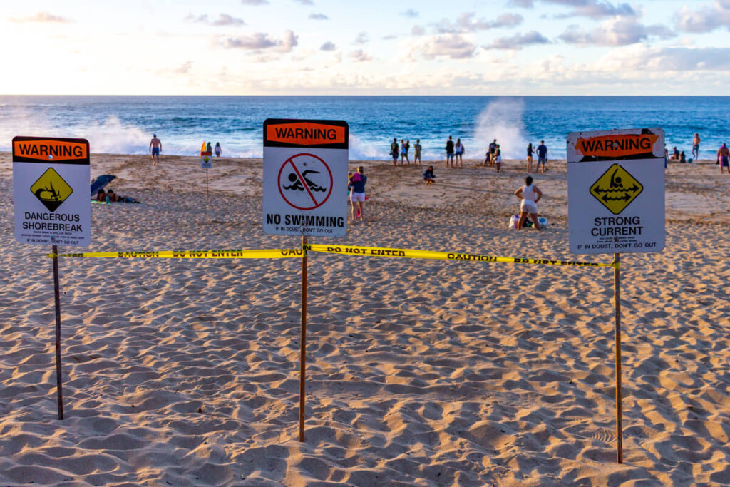warning signs against swimming and large waves at Waimea Bay Beach Park on North Shore of Oahu