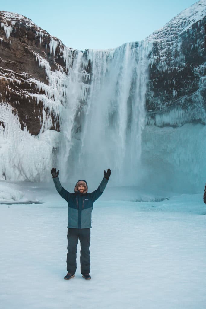 guy standing in front of waterfall in Iceland in winter
