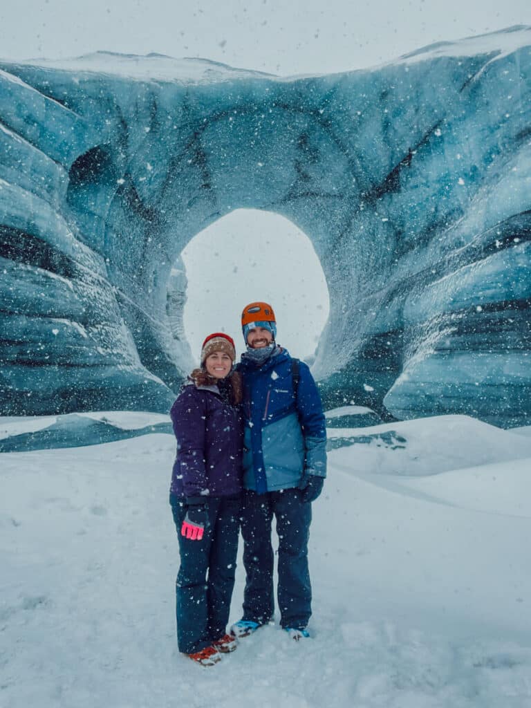 couple standing in front of Katla Ice Cave in Iceland during winter.