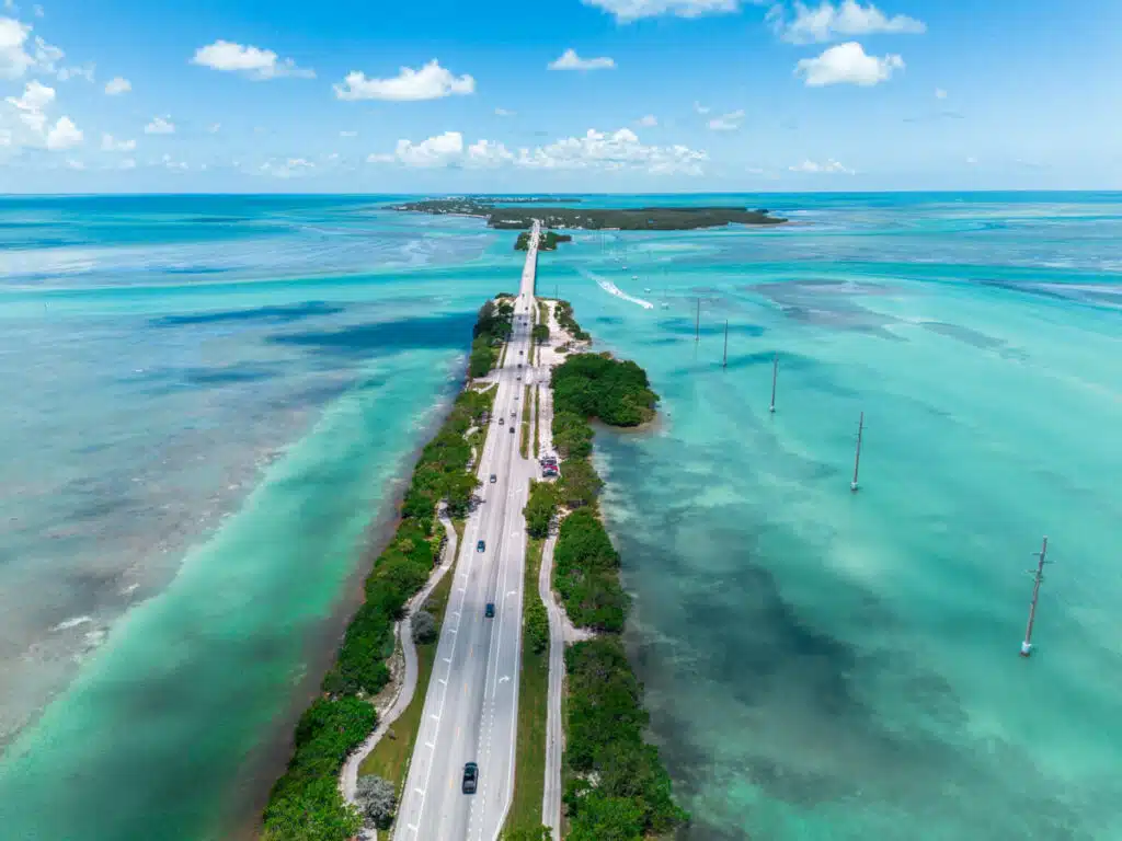 Highway US-1 cutting through the vivid aqua waters of Islamorada, Florida Keys, with cars traveling along a narrow strip of land flanked by the ocean on both sides.