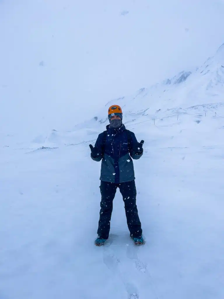man in helmet and winter gear surrounded by snow giving two thumbs up to the camera on the way to the Katla Ice Cave