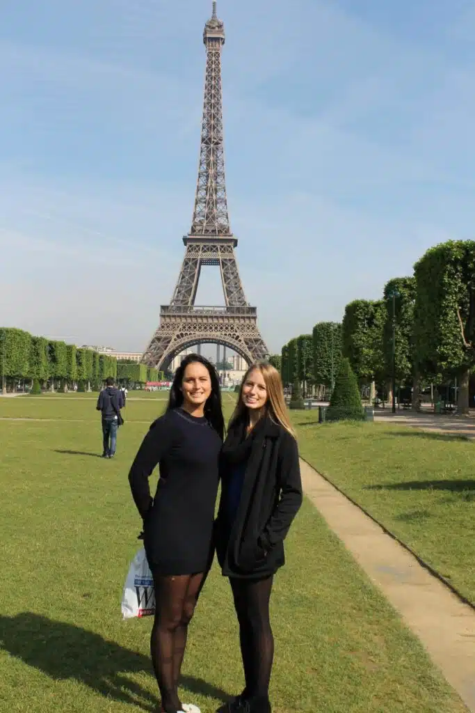 two girls standing in front of the Champ de Mars greenspace in front of Eiffel Tower in Paris, France