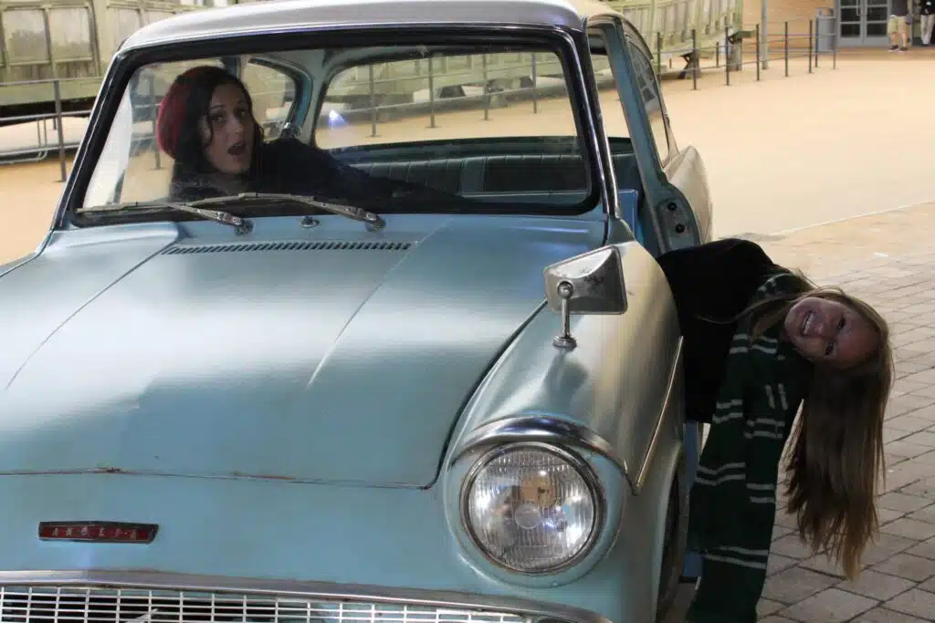 Playful moment with one woman sitting in the flying Ford Anglia car and another leaning out at the Warner Bros. Studio Tour London, a magical and whimsical thing to do in London