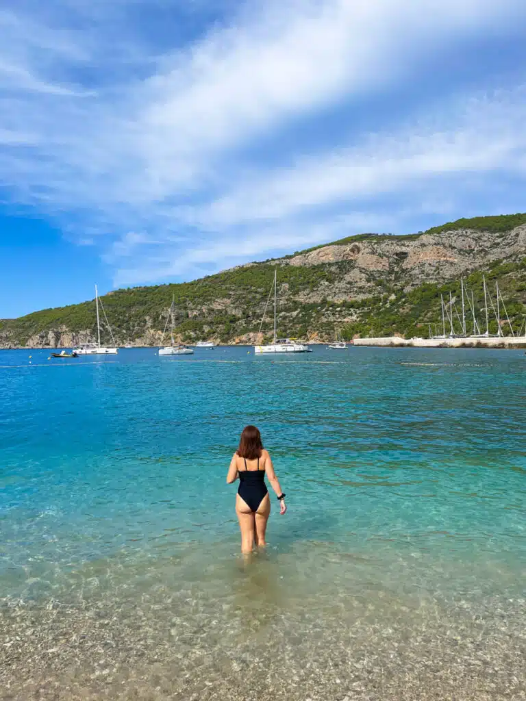 girl walking into blue water on a beach in Vis, Croatia with moutains in the background