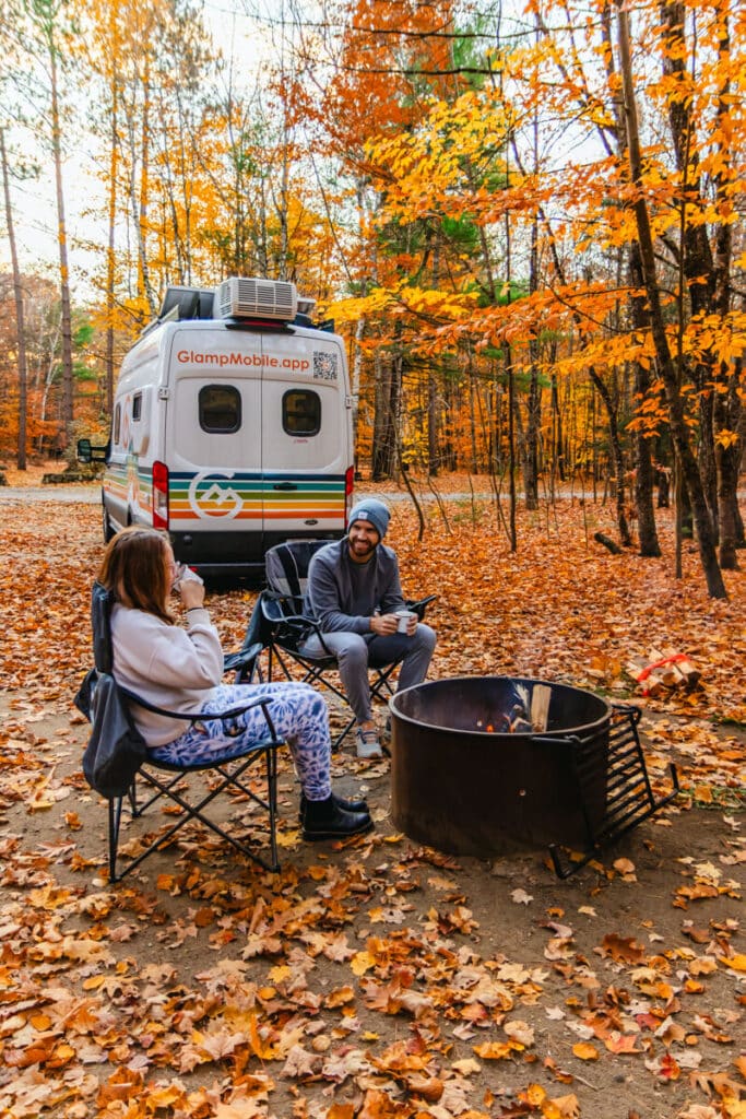 couple sitting in front of firepit and van in White Mountains National Forest in New Hampshire
