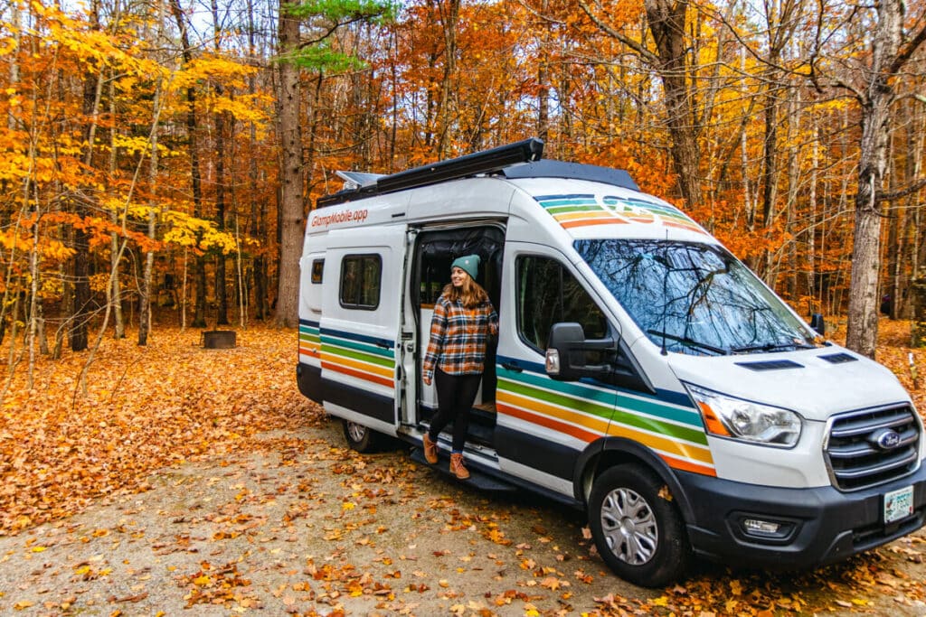 girl leaning out of campervan surrounded by fall foliage in in White Mountains National Forest in New Hampshire