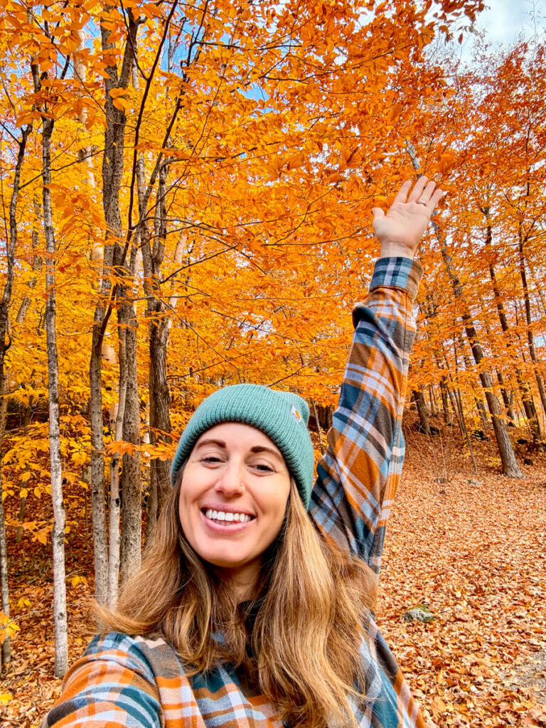 girl smiling at camera with hand in air in front of orange trees in in White Mountains National Forest, New Hampshire