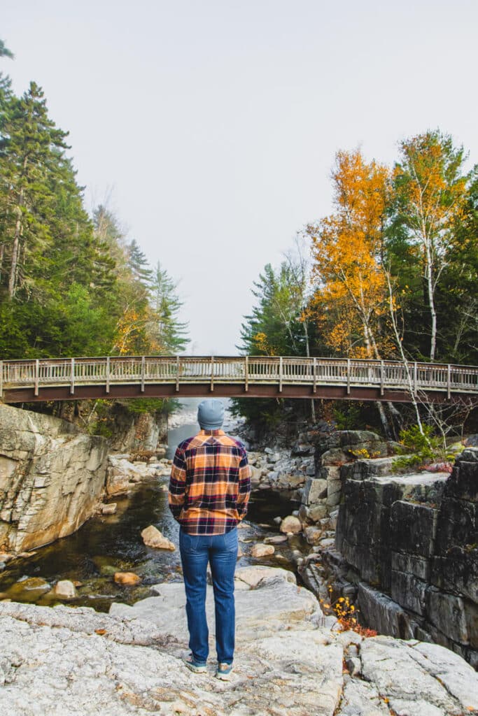 man in plaid standing in front of Rocky Gorge bridge in White Mountains New Hampshire