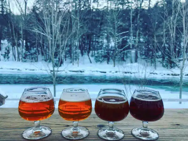 glasses of beer on wood plank in front of snowy riverbank at Long Trail Brewing Company in Woodstock, VT