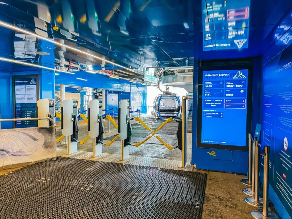 Entrance to the Matterhorn Express gondola station in Zermatt in winter, with automated gates, ticket screens, and a gondola cabin waiting to transport visitors up the snowy mountains.