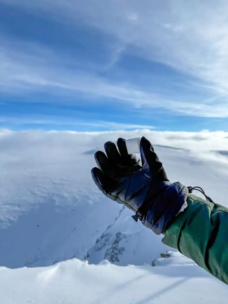 black gloved hand holding snow in the shape of a cube with blue sky and snowy mountain in the background. Taken at the top of the Matterhorn Glacier Paradise in Zermatt, Switzerland