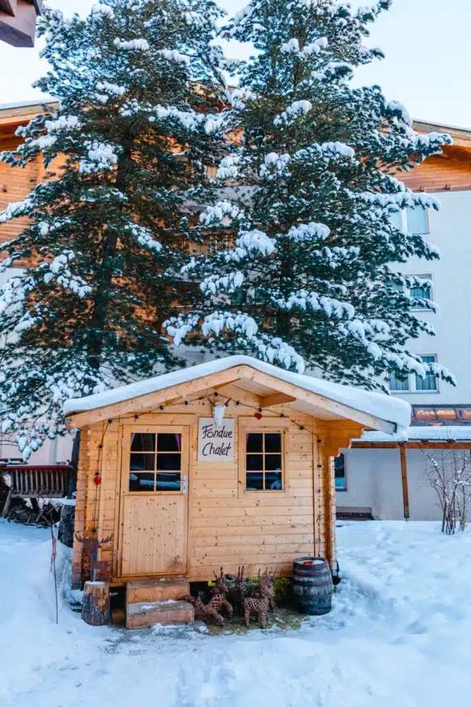 cozy wooden fondue chalet surrounded by snow with pine trees in the background