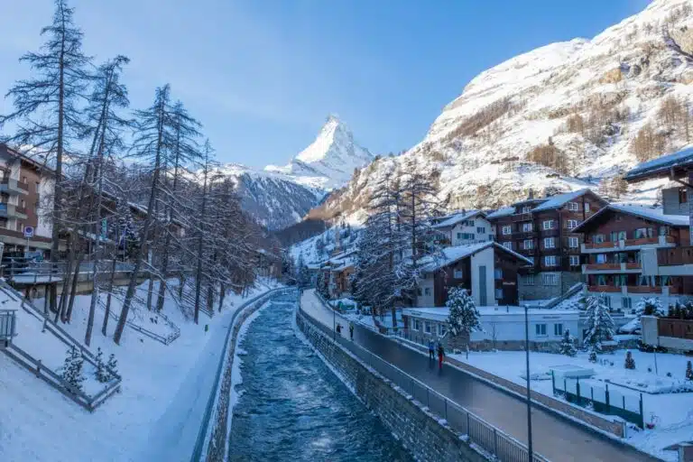 icy river in the middle of snowy town with matterhorn in the background and blue skies