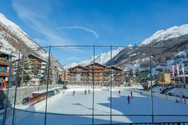 people iceskating on ice rink with wooden hotels in the background in Zermatt, Switzerland-min