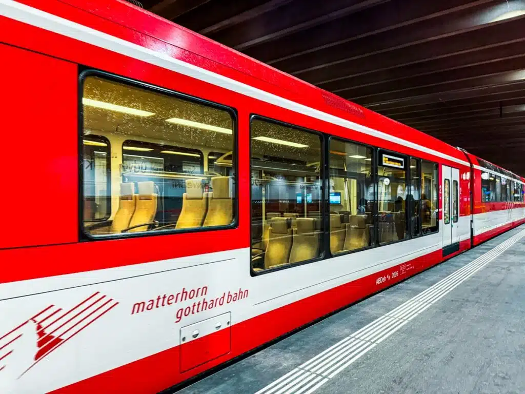 red and white train with large windows and Matterhorn Gothard Bahn on side in Zermatt train station-min