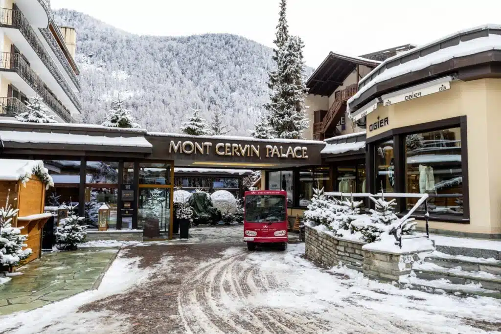snowy hotel entrance with red truck in front and snowy trees in background in Zermatt, Switzerland