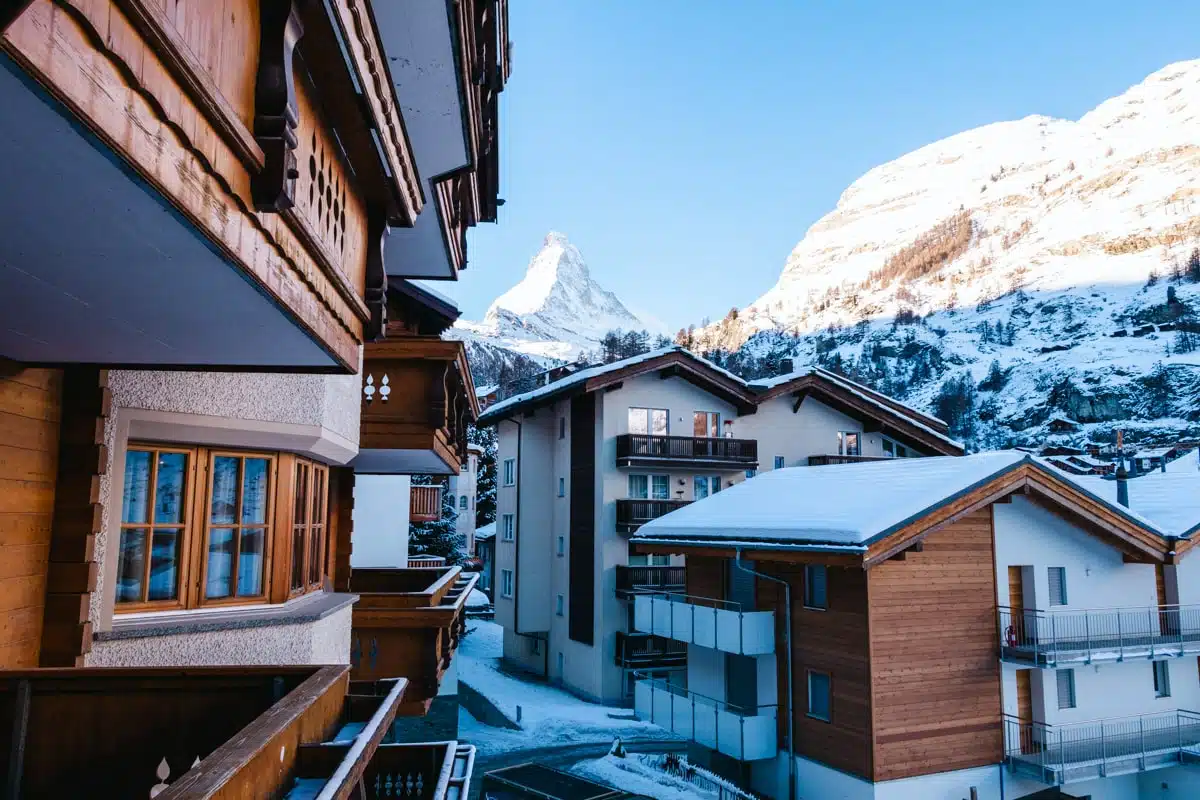 view of snow-covered matterhorn from wooden hotel balcony with snowy buildings in the foreground in Zermatt, Switzerland