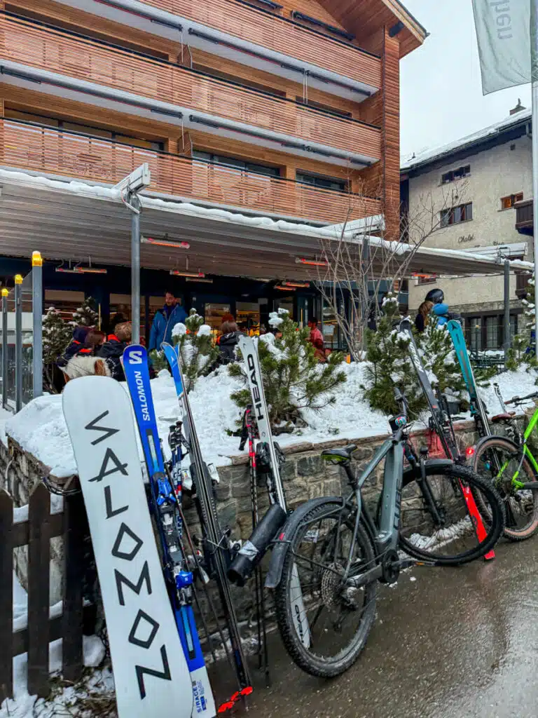 Skis, a snowboard and bikes leaned against a snowy wall outside the heated après-ski terrace at Hotel Zermama in Zermatt