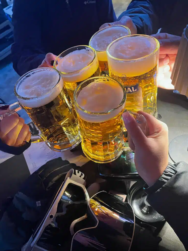 Group clinking mugs of beer over ski goggles and gloves during après-ski at Hotel Zermama in Zermatt, Switzerland