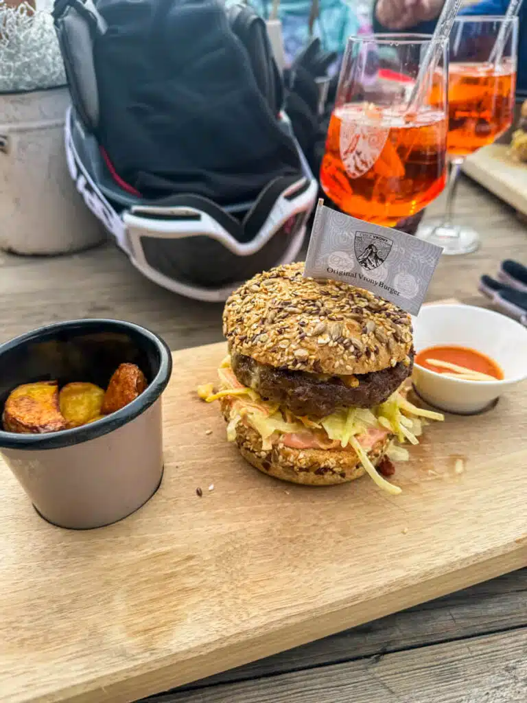 Original Vrony Burger with roasted potatoes and Aperol spritzes on a wooden board at Chez Vrony in Zermatt