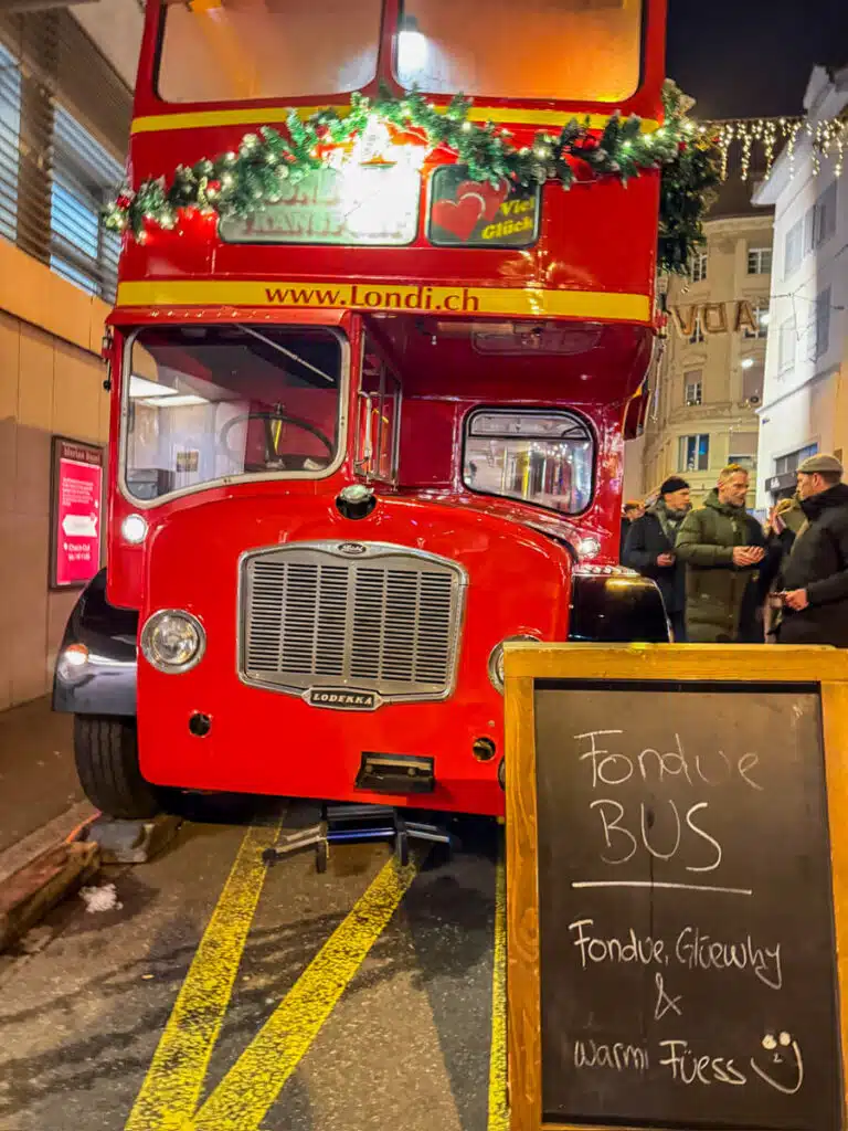 Front of the red double-decker Fondue Bus with a chalkboard sign for fondue and glühwein at the Adväntsgass market in Basel
