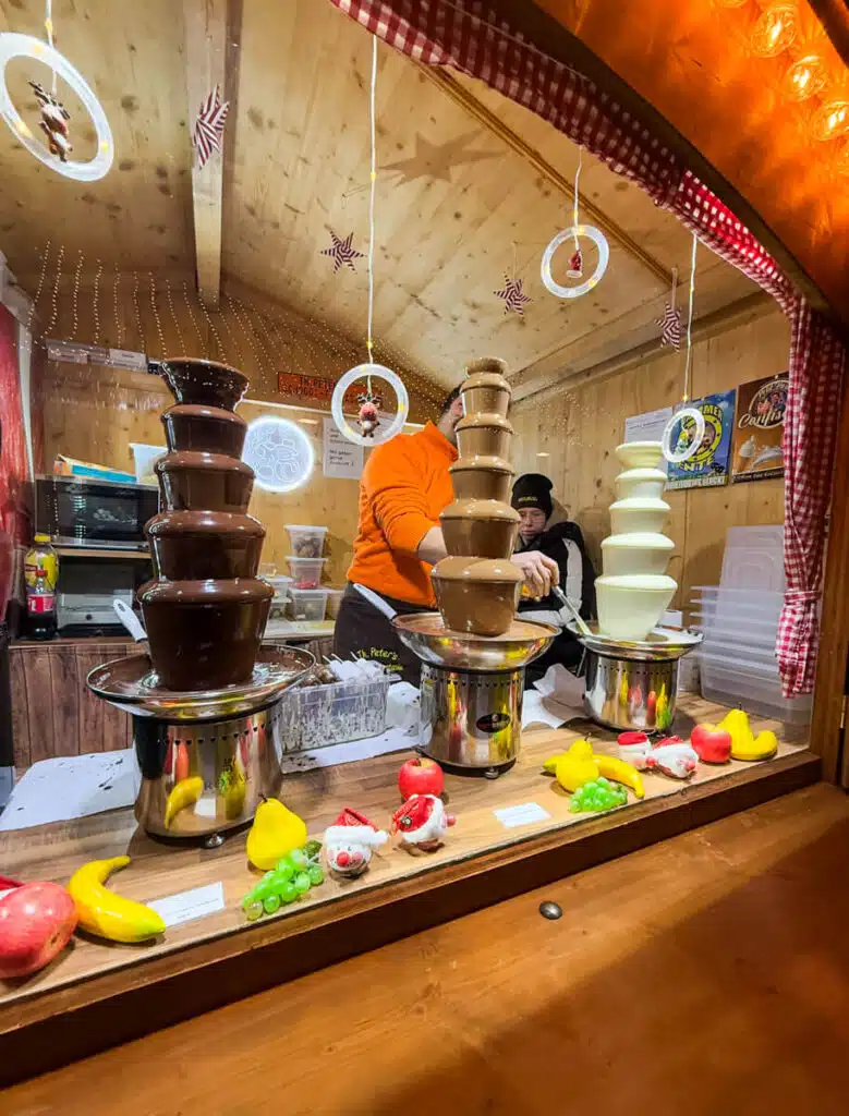 Milk, dark and white chocolate fountains with fruit at a wooden stall at the Basel Barfusserplatz Christmas market