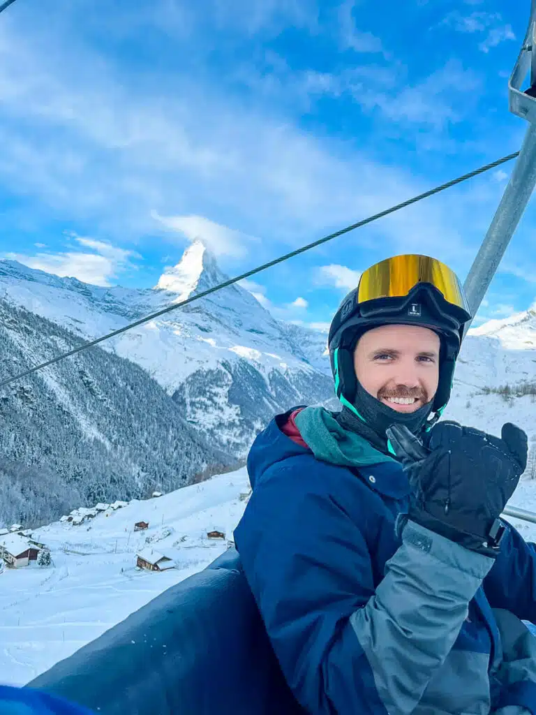 Snowboarder smiling on a chairlift above Zermatt’s Sunnegga slopes with the snow-covered Matterhorn behind him