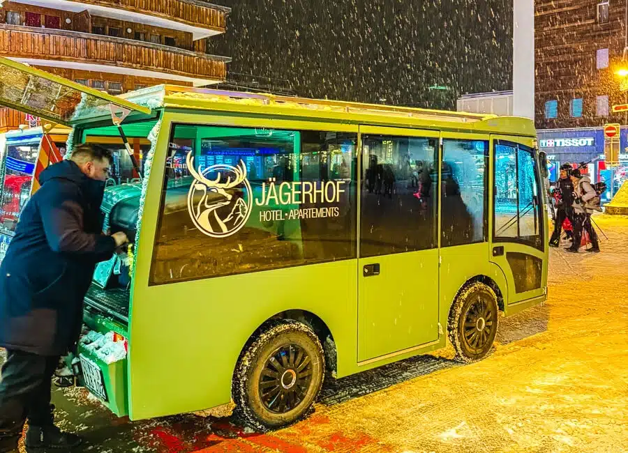 green e-shuttle in zermatt Switzerland outside train station with man loading suitcases in as snow falls.