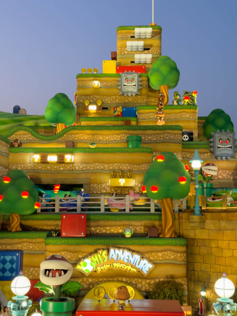 The glowing, colorful facade of Yoshi’s Adventure at Super Nintendo World is filled with characters, trees, coins, and platforms from the Mario games.