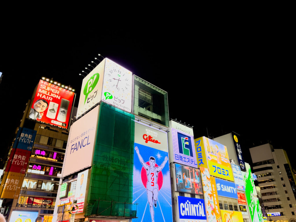 The famous Glico Running Man sign lights up the night at Dotonbori in Osaka, surrounded by bright LED billboards and advertisements.