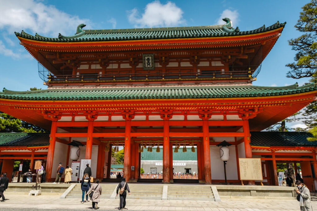 Heian Jingu Shrine in Kyoto featuring bright vermilion wooden pillars white walls and green tiled roofs beneath a blue sky.