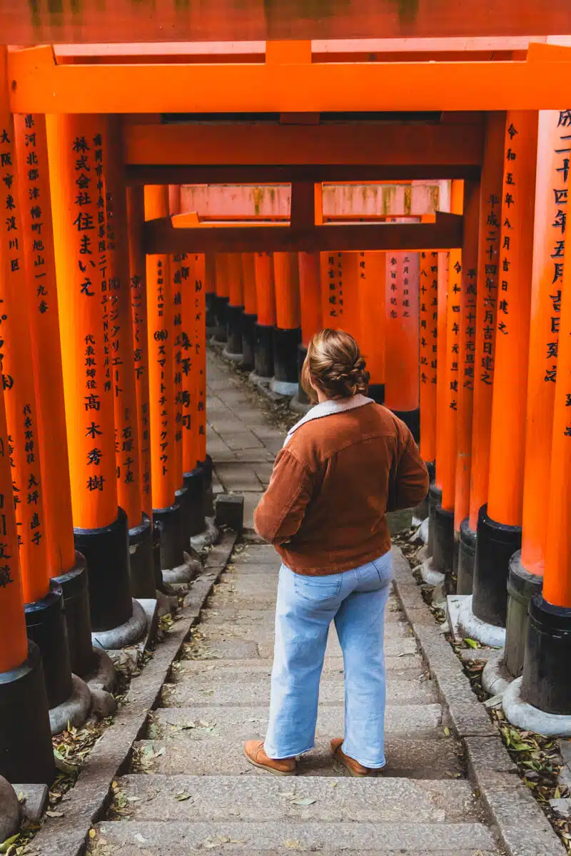 girl standing on stairs of Fushimi Inari, Kyoto, Japan surrounded by red torii gates