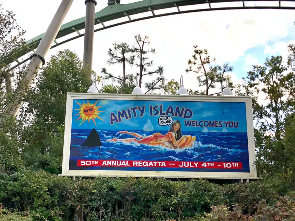 Billboard at Universal Studios Japan in Osaka reading "AMITY ISLAND WELCOMES YOU" and "50TH ANNUAL REGATTA JULY 4TH 10TH" showing a swimmer in the ocean with a shark fin approaching in a Jaws themed design.