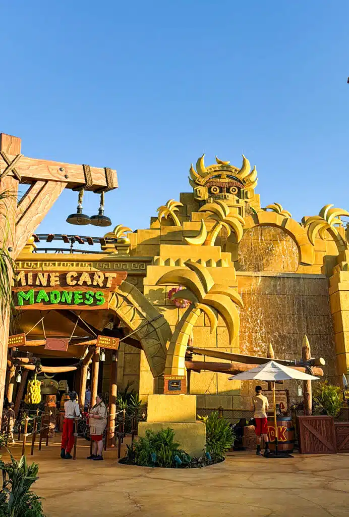 Entrance to "Mine Cart Madness" at Universal Studios Japan in Osaka featuring a large golden temple style facade with a waterfall and carved face above the ride entrance as visitors walk inside.