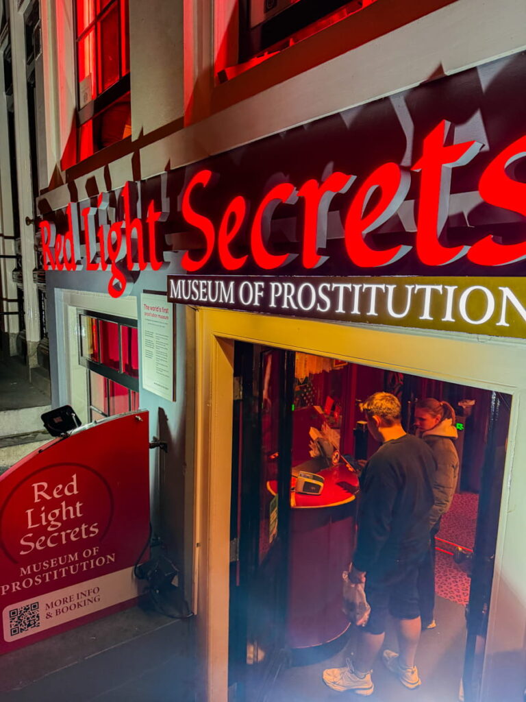Entrance to "Red Light Secrets Museum of Prostitution" glowing with bright red neon lights as visitors stand at the doorway. This museum offers insight into the area’s history and is a unique stop on an Amsterdam itinerary.