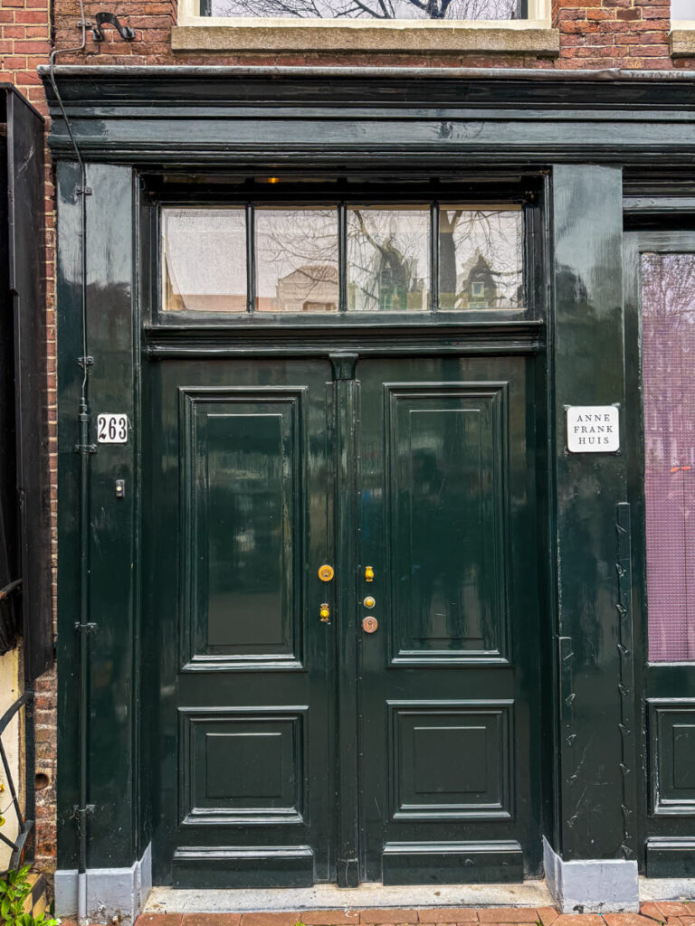 Dark green entrance door with a small sign reading "Anne Frank Huis" beside it marking the old entrance to the Anne Frank House. Visiting this location is a meaningful experience on an Amsterdam itinerary.