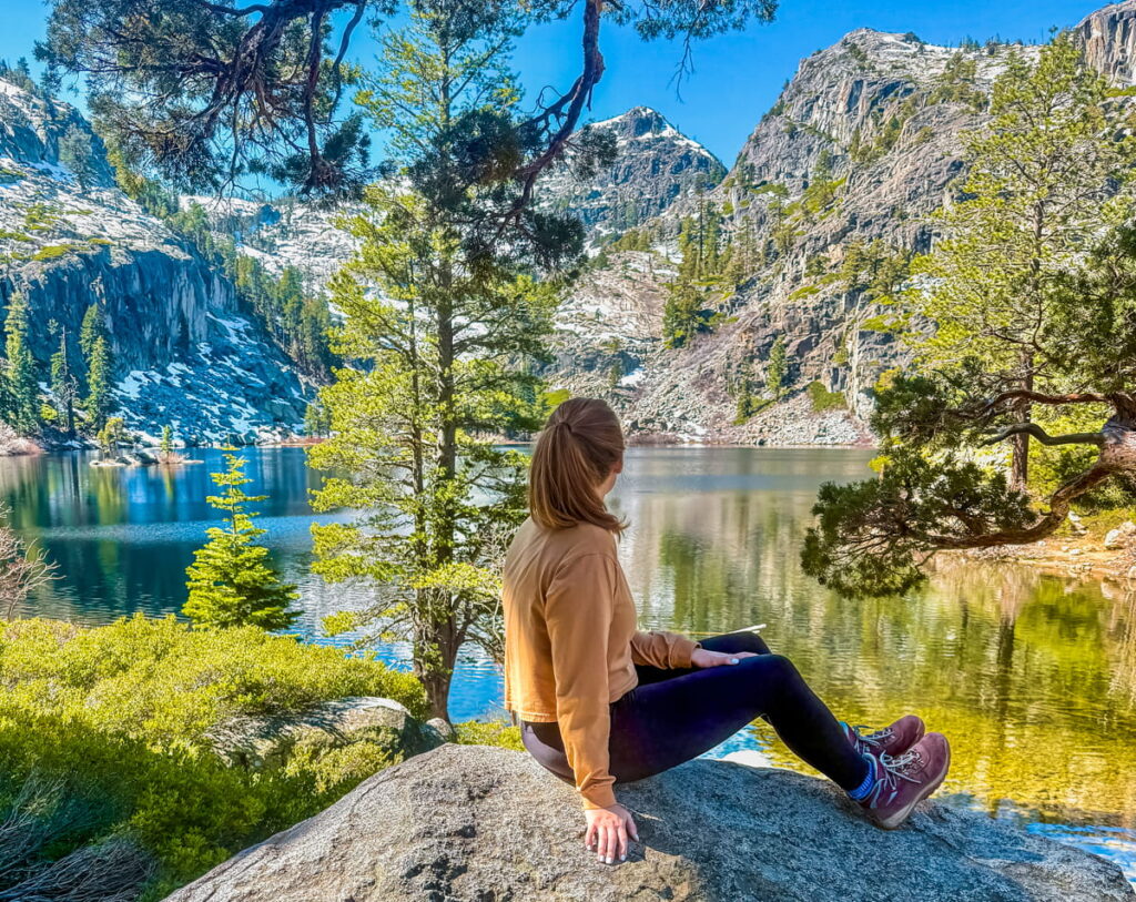 girl sitting on rock looking away from camera towards Eagle Lake in the background, with greenery and mountains surrounding her