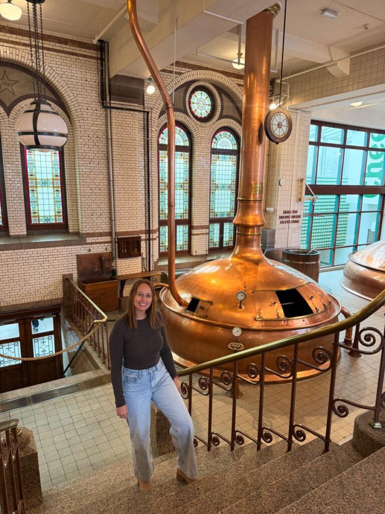 Large copper brewing tanks inside the historic Heineken brewery with a woman standing on the steps beside them.