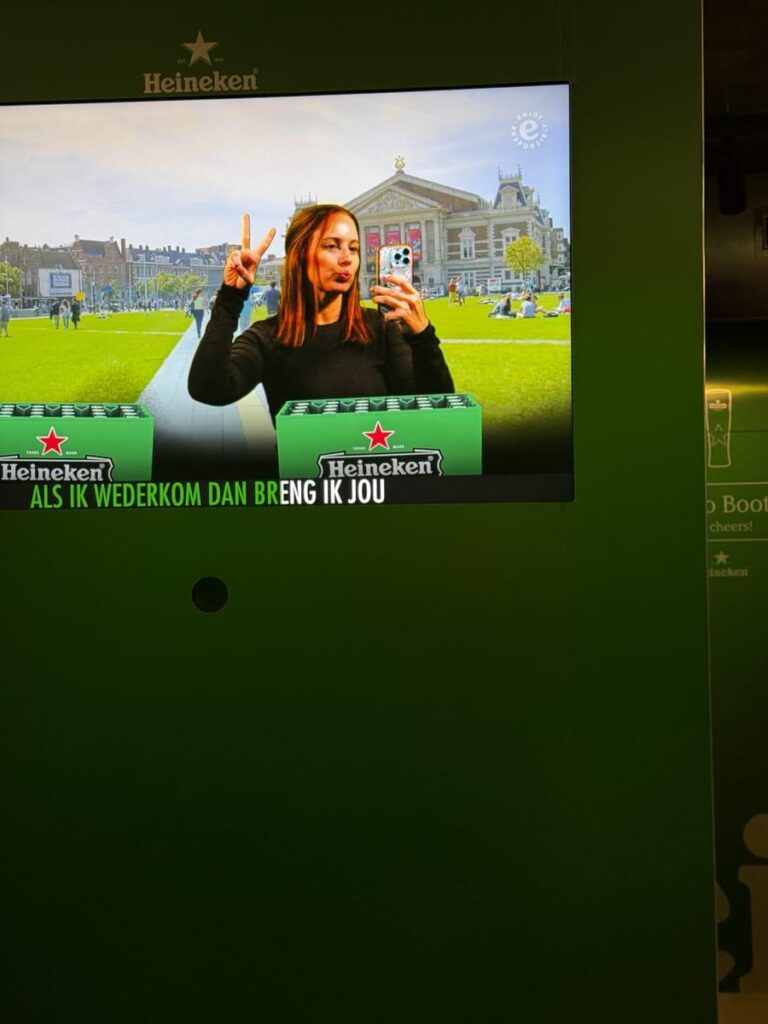 Screen showing a woman posing with a peace sign in front of a green Heineken themed photo booth background.