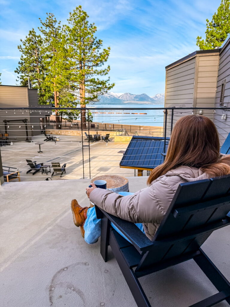 girl sitting on a chair with a coffee cup in hand on the balcony of her room at the Landing Resort and Spa in Lake Tahoe, looking at the lake in the background