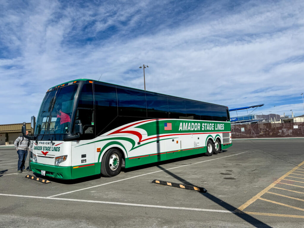 Green and white coach bus parked in a lot with "Amador Stage Lines" written on the side as a driver stands nearby. This is the South Tahoe Airporter shuttle bus from the airport.