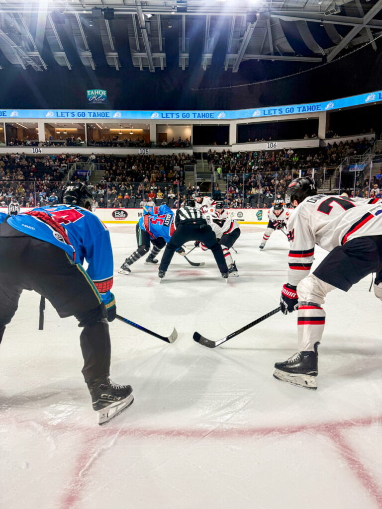 two hockey players squat next to each other, with more players and a ref in front of them during a face-off at a Tahoe Knight Monsters game