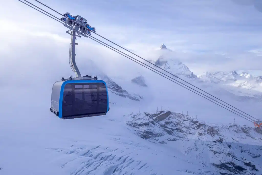 blue ski gondola on a cable up the mountain with the snowy matterhorn in the background