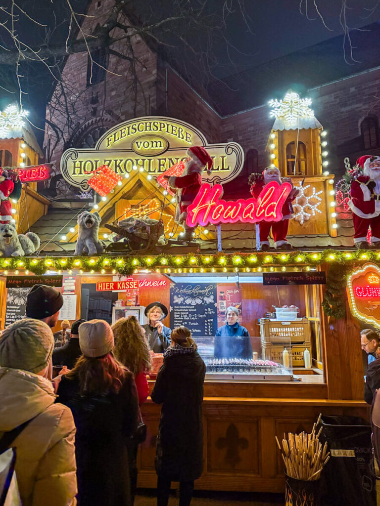 Christmas market food stall selling grilled meat skewers, decorated with Santa figures and neon lights. Taken at the Basel Munsterplatz Christmas Market in Switzerland